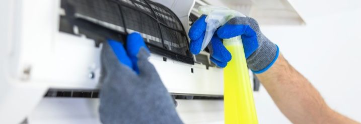 Person reinigt Klimaanlage mit Sprühflasche.